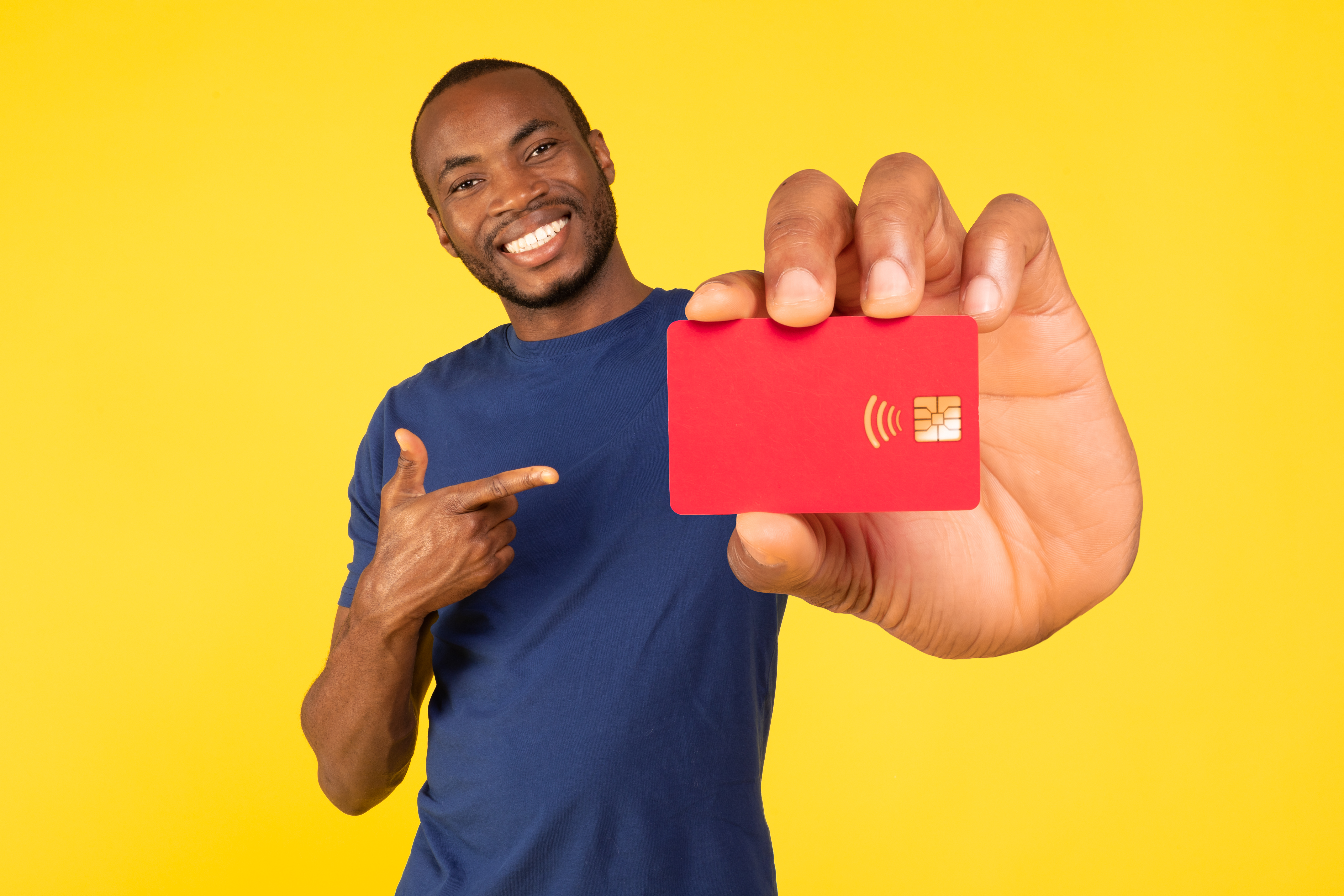 Cheerful African American Guy Showing Credit Card Pointing Finger Recommending Bank Offer Smiling To Camera Standing On Yellow Studio Background. Check This Offer Concept